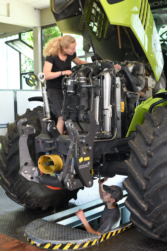 Zwei junge Land- und Baumaschinemechatroniker bei der Arbeit am Motor eines Traktors.