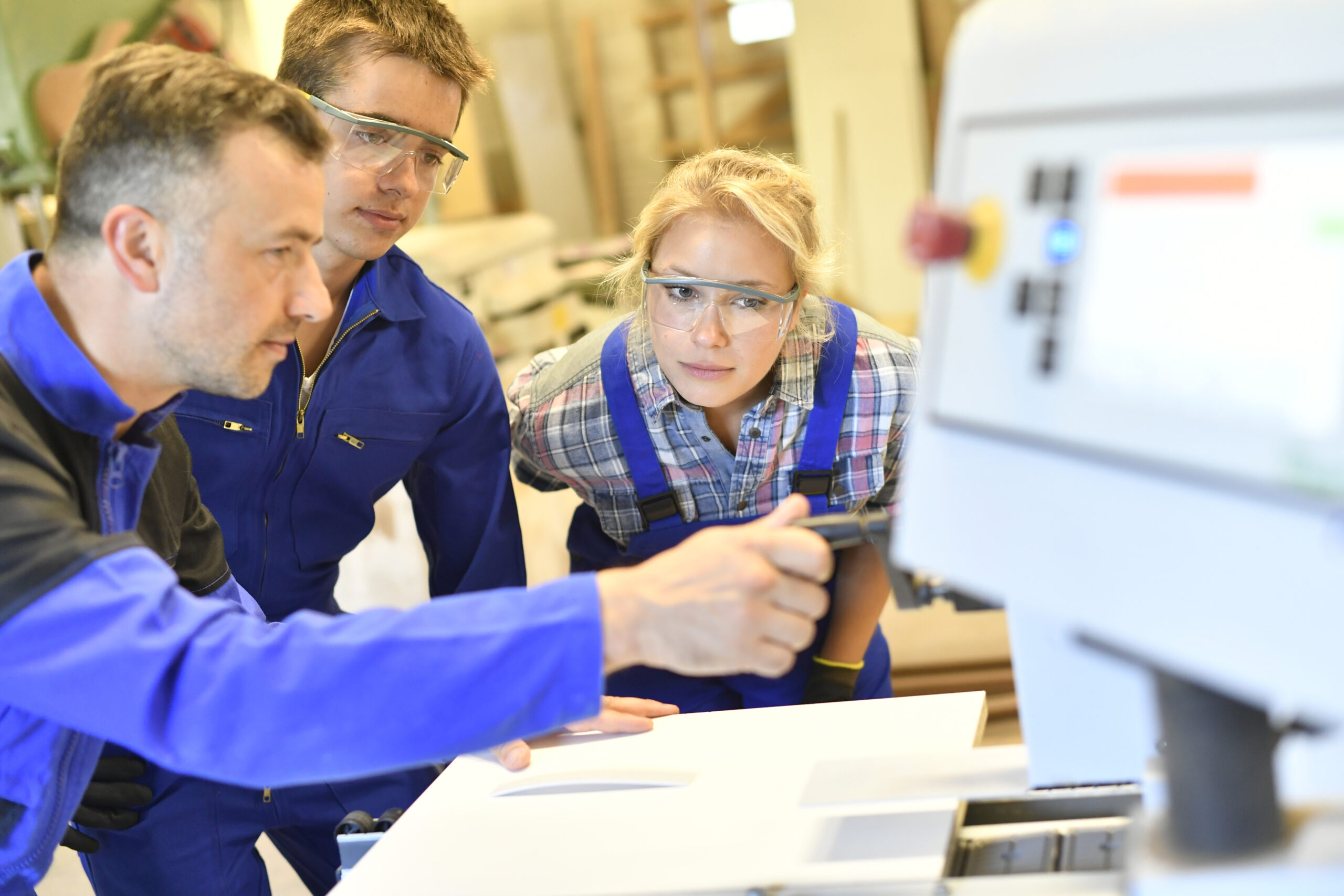 Professor erklärt zwei Studenten die Arbeit an einer Maschine.