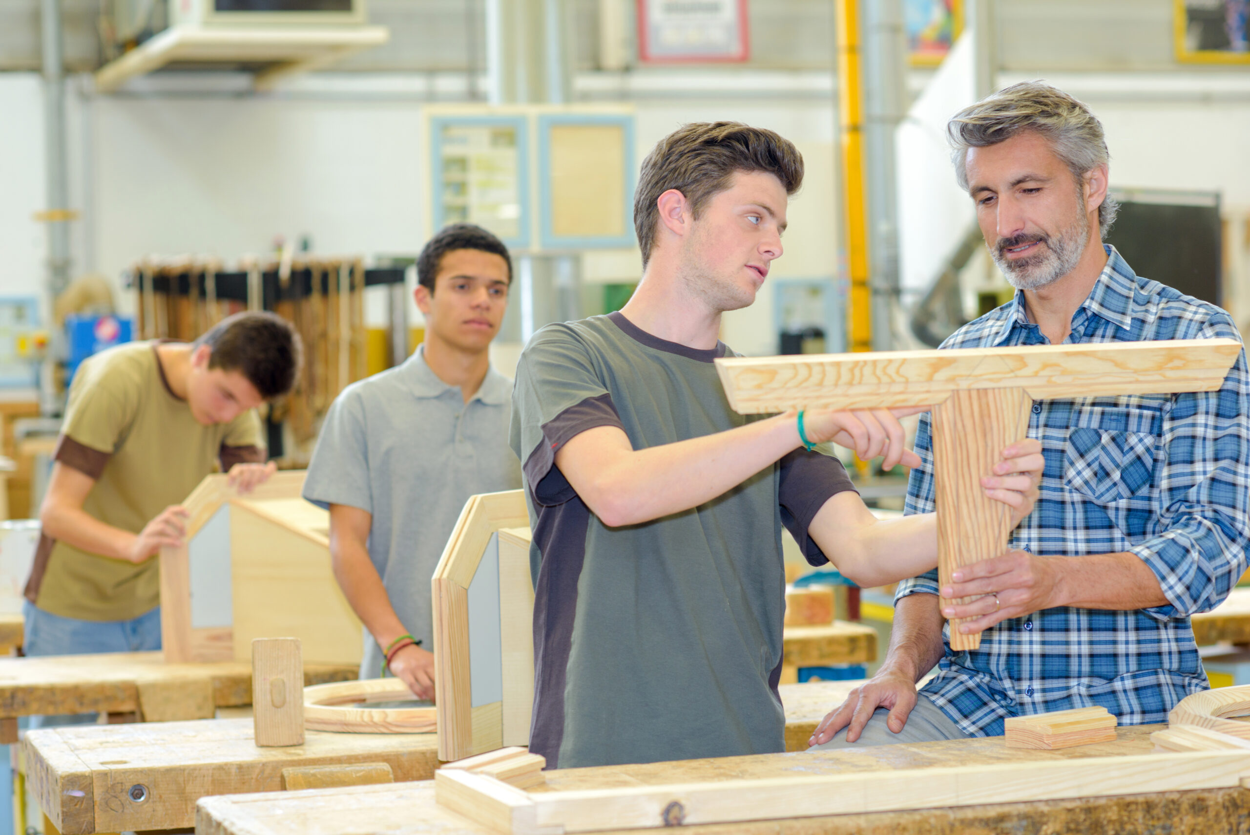 Studenten mit Professor in einer Werkstatt beim Fertigen von Holzwerkstücken