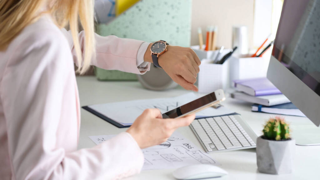 Frau guckt im Büro auf die Uhr - Zeitstress im Arbeitsalltag